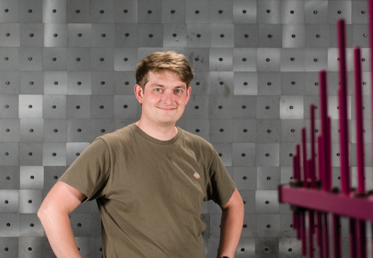 Das Foto zeigt Robert Nowak in einem T-Shirt in einer Absorberkammer stehend. Am Rand des Bildes sieht man unscharf eine Antenne, welche auf Ihn ausgerichtet ist.